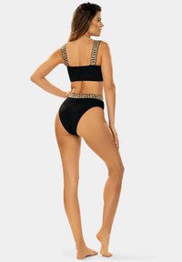 Czarny bikini z złotym wzorem greckiego klucza na ramiączkach i pasku. Gładki materiał; dopasowany krój z wysokim stanem majtek i wspierającym topem.