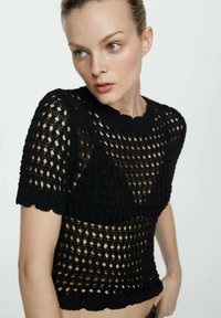 Zwarte gebreide crop top met een gestructureerd open geweven patroon, korte mouwen en een gekartelde zoom voor een uniek ontwerp.