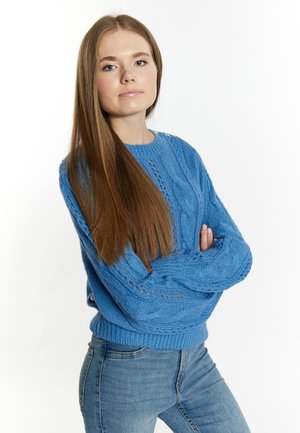 Blauwe gebreide sweater met kabelpatronen en een geribbelde zoom. Lange mouwen met textuurdetails. Gecombineerd met straaltje blauwe jeans.