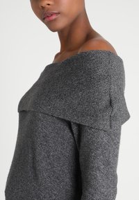 Grauer schulterfreier Pullover mit strukturiertem Strickdesign, lockerer Passform und breiten Bündchen. Weicher Stoff wirkt gemütlich und warm.