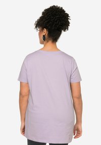 Camiseta corta de manga corta de color púrpura claro con un ajuste holgado, escote redondo y textura de algodón suave, vista desde la parte posterior.