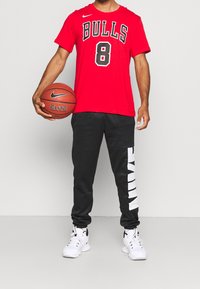 T-shirt rossa dei Bulls della Nike con scritte nere e numero 8, abbinata a pantaloni jogger neri con il marchio Nike bianco lungo il lato. Sneakers bianche.