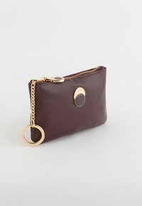 Bolso de cuero marrón con cremallera dorada y detalle circular en el herraje. Cuenta con una cadena para facilitar su transporte. Acabado texturizado.