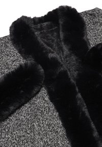 Collo e polsini in pelliccia sintetica nera dettagliati su un tessuto grigio intrecciato con texture. Il cappotto presenta un design semplice e aperto senza chiusure.