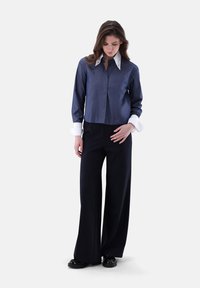 Dark blue cropped shirt with a white collar and cuffs, paired with wide-leg black pants. The fabric appears smooth and tailored.