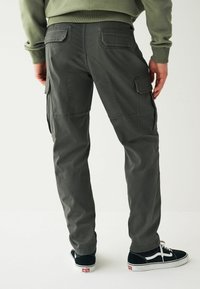 Dunkelgraue Cargo-Hosen mit Seitentaschen, geradem Bein-Design und Nähdetails. Kombiniert mit schwarzen Sneakers mit weißen Sohlen.