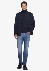 Marinejakke over en marineblå turtleneck, parret med lyseblå jeans og sorte dressko. Glat stof og skræddersyet pasform.