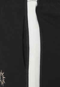 Zwarte shorts met een witte zijstreep, gemaakt van zachte stof. Opvallend detail is een beige zonafbeelding aan de voorkant.