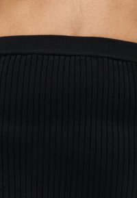 Κοντινό πλάνο μέσης με ρούχο από μαύρο, ριμπ ύφασμα με ψηλή μέση, πάνω σε γυμνό δέρμα.