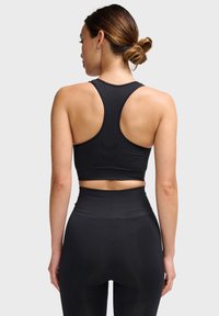 Zwarte atletische crop top met een racerback ontwerp en een zachte textuur, gecombineerd met hoge zwarte leggings met een gestructureerd patroon.