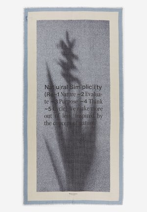 Rektangulært stof med lyseblå kant, tekstureret gråt centrum, skygge af en plante og delvist synlig tekst om naturlig enkelhed.