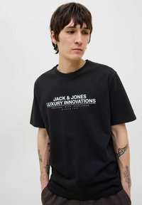 Svart bomullströja med vit text: "JACK & JONES LUXURY INNOVATIONS" och ytterligare detaljer. Kort ärm, avslappnad passform.