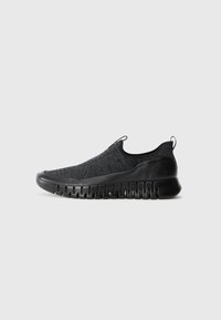 Black slip-on sneakers featuring a textured knit upper and a rubber sole with a wave pattern. Minimalist design with no visible laces.