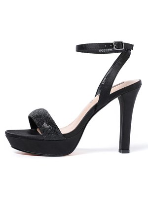 Czarna sandałka na wysokim obcasie z grubym paskiem wokół kostki, szerokim paskiem na palcach i fakturowaną górą. Obcas ma około 10 cm, podeszwa gruba na 2 cm.