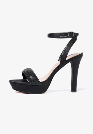 Czarna sandałka na wysokim obcasie z grubym paskiem wokół kostki, szerokim paskiem na palcach i fakturowaną górą. Obcas ma około 10 cm, podeszwa gruba na 2 cm.