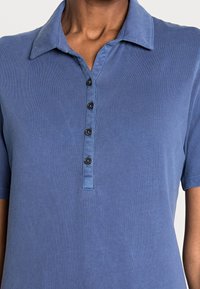 Camisa polo de manga corta y cuello en algodón de color azul claro, con una tapeta de botones que presenta cinco botones negros y una textura suave.