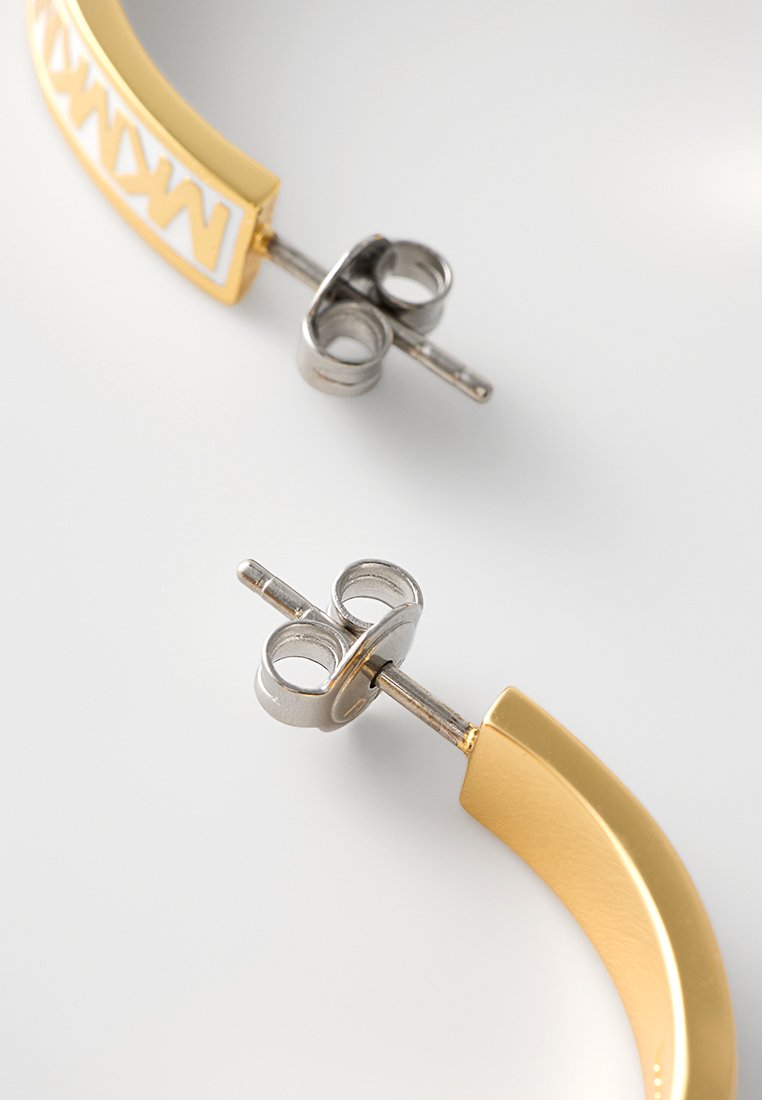 Pendientes de aro de metal dorado con un diseño liso y curvado. Presenta un acento blanco y cierres en tono plateado para un ajuste seguro.