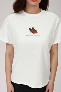 White cotton t-shirt featuring a butterfly graphic in orange and black, with the text "WINGS OF CHANGE GOOD THINGS ARE COMING" below.