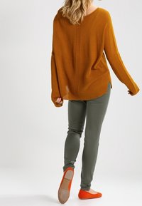 Sinapinkeltainen neulepaita, jossa keskellä teksturoitu sauma, yhdistetty oliivinvihreisiin istuviin housuihin ja oransseihin balleriinakengiin.