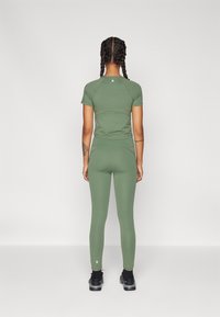 Žalias sportinis topas ir leggingai, pagaminti iš elastingos medžiagos, su prigludusia forma. Aprangoje yra minimalus logotipo detalė šalia apvado.