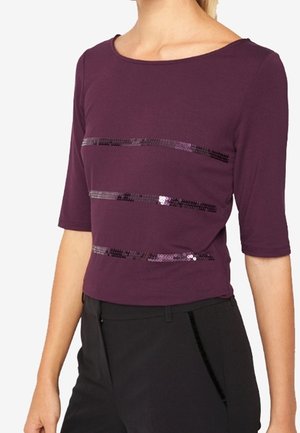 Top violet à manches courtes en tissu doux, présentant des rayures de sequins horizontales pour des accents décoratifs. Associé à un pantalon noir.