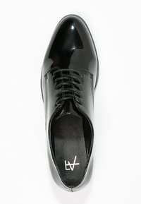 Chaussure en cuir verni noir à lacets avec un bout arrondi, surface lisse et couture décorative le long de l'empeigne. Semelle intérieure texturée visible.