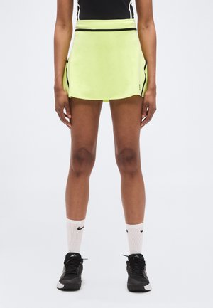 Neon yellow athletic skirt with a flared design, black trim, and side pockets, paired with white Nike socks and black sneakers.