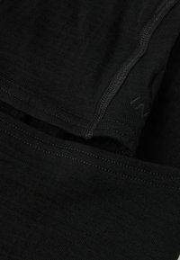 Mustast tekstureeritud kangast lähedalt vaadatuna, nähtavate õmblustega ja kattuvate õmblusõmblustega.