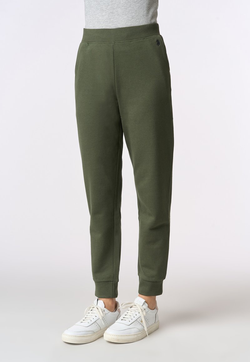Pantaloni felpati verde scuro con polsini aderenti alla caviglia, realizzati in morbido tessuto, caratterizzati da tasche laterali e un discreto dettaglio del logo.