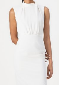 Robe blanche sans manches avec un col montant et une taille froncée. Tissu lisse et extensible créant une silhouette ajustée. Design simple et élégant.