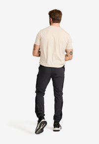 Beige kortärmad skjorta i kombination med svarta cargo-byxor med avsmalnande anklar. Svartvita sportskor fulländar outfiten.
