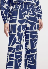 Marineblauwe en witte gedessineerde broek met brede pijpen en een elastische tailleband. Bevat geometrische vormen in verschillende maten verspreid over de stof.