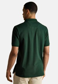 Tume roheline polo särk, mis sisaldab klassikalist krae, lühikesi varrukaid ja pehmet tekstuuri. Tähtsad külgsisselõiked hemil suurendavad mugavust.