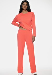 Laxfärgad långärmad topp som matchas med vida byxor i samma färg, tillverkade av mjukt tyg, med en avslappnad passform och enkel design.