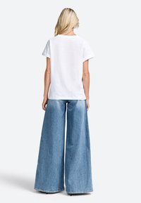 T-shirt en coton blanc à manches courtes associé à un pantalon en jean bleu clair à jambes larges, avec un ourlet brut et une coupe décontractée.