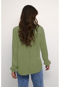 Lange mouw, lichtgroene blouse van doorschijnende stof, met een ontspannen pasvorm en manchetmouwen, gedragen met blauwe denim jeans.