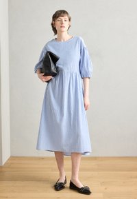 Blå og hvit stripete kjole med korte pufferm, en samlet midje og en utsvingt skjørt, kombinert med en svart clutch og flate sko.
