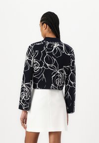 Ναυτικό μπλέιζερ με λευκό floral σχέδιο, στρογγυλή λαιμόκοψη, μακριά μανίκια, κοντή σχεδίαση, συνδυασμένο με λευκή φούστα, λεία υφή.