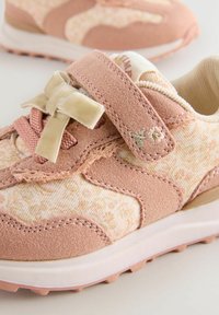 Rosa mockaskinn och blommönstrad tygsneaker med klädd rem, dekorativ rosett och kontrasterande vit sula, med lätta greppmönster.