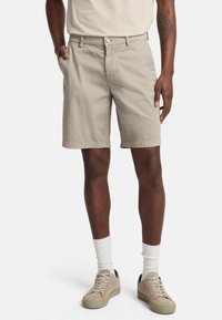 Beige katoenen shorts met een rechte pasvorm, zijzakken en een knoopsluiting. Gepaard met lichte sneakers en witte sokken.