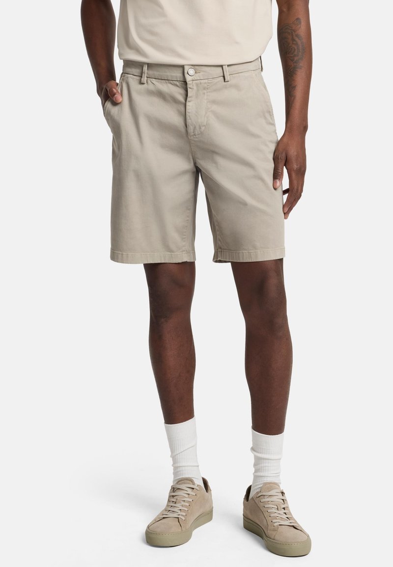 Beige katoenen shorts met een rechte pasvorm, zijzakken en een knoopsluiting. Gepaard met lichte sneakers en witte sokken.