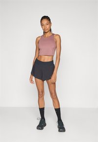 Mauvu krāsas īsi tops, augsta darbības josta melnā šortos, saskaņots ar melnām zeķēm un sporta apaviem. Izceļas ar pieguļošu dizainu un mīkstu tekstūru.