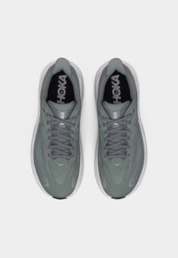 Ζευγάρι γκρι αθλητικών παπουτσιών Hoka με μαύρες εσωτερικές σόλες και λευκές μεσαίες σόλες, που φαίνεται από πάνω σε λευκό φόντο.