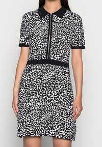 Robe à manches courtes imprimée léopard noir et blanc, avec une fermeture éclair à l'avant et une coupe ajustée, dotée d'une ceinture noire unie.