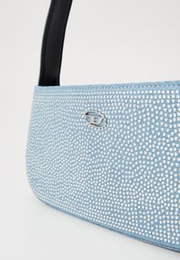 Borsa a mano blu chiaro con superficie testurizzata decorata con piccoli rivetti metallici, dotata di una tracolla nera e un accento logo argentato.