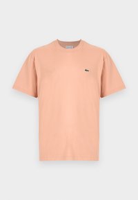 Tricou din bumbac, cu mâneci scurte și guler rotund, de culoare piersică deschisă, cu un mic logo verde al crocodilului Lacoste pe pieptul stâng.