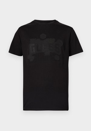 Černé bavlněné tričko s krátkými rukávy a kulatým výstřihem. Obsahuje tónovaný reliéfní design loga "GUESS", zdůrazněný dekorativními prvky.