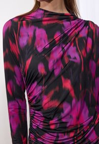 Maglietta a maniche lunghe in un vivace motivo nero, rosa e rosso. Presenta un design drappeggiato con dettagli arricciati su un lato. Tessuto dalla superficie morbida.