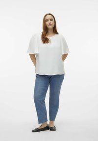 Witte top met textuur en sleutelgatdetail, korte fluttermouwen, gecombineerd met lichtblauwe jeans en zwarte platte schoenen op een effen achtergrond.