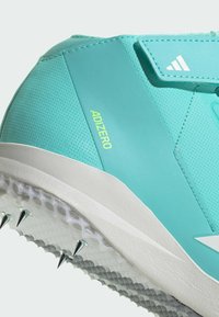 Scarpa da corsa azzurro chiaro con parte superiore testurizzata, logo "ADIZERO" ben visibile, suola bianca con spike a vista e design elegante e aerodinamico.